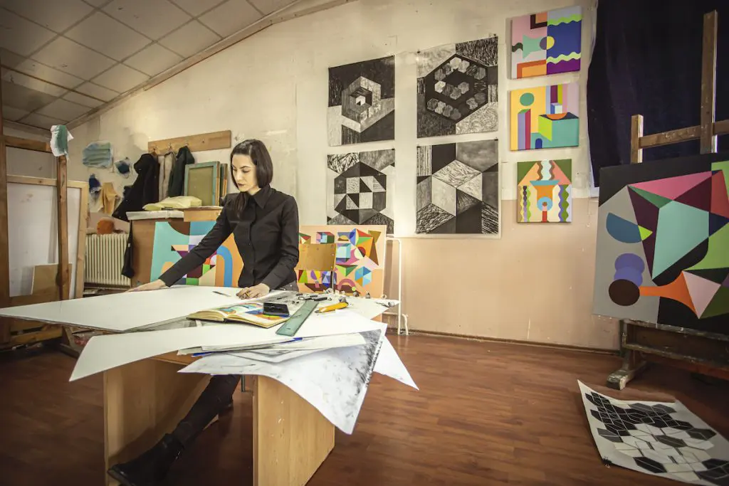 A woman working in her art studio with artwork on the walls.